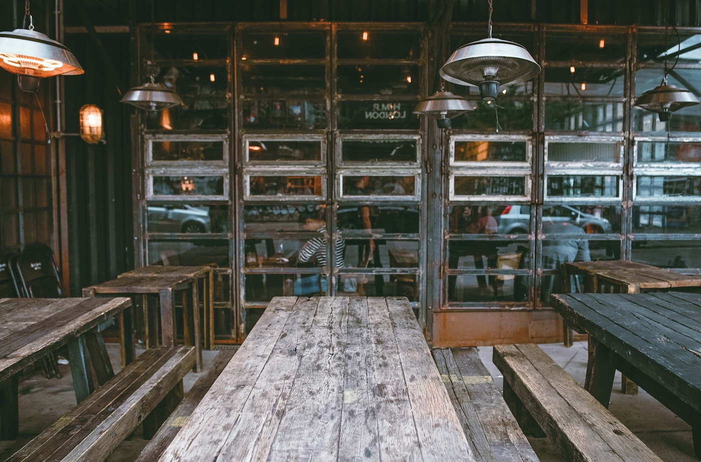 Comedor exterior con mesas rústicas de madera y lámparas colgantes frente a ventanales